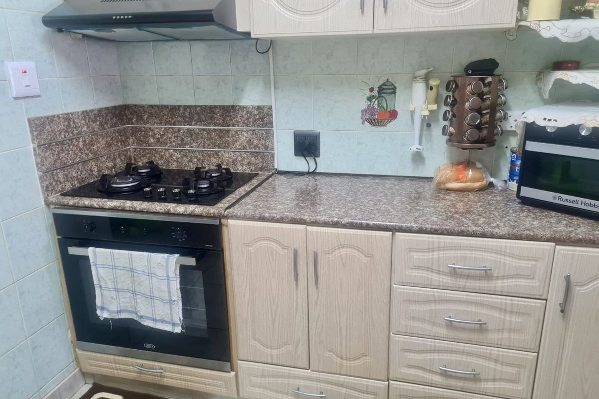 A functional kitchen area featuring built-in cabinetry, a gas hob, an integrated oven, and an extractor fan with tiled splashbacks.