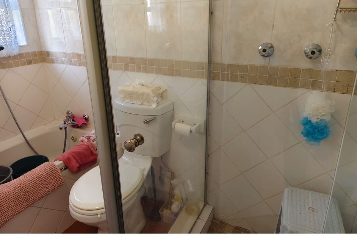 A functional bathroom featuring a combined shower and bathtub unit, a standard toilet, and neutral wall tiling.