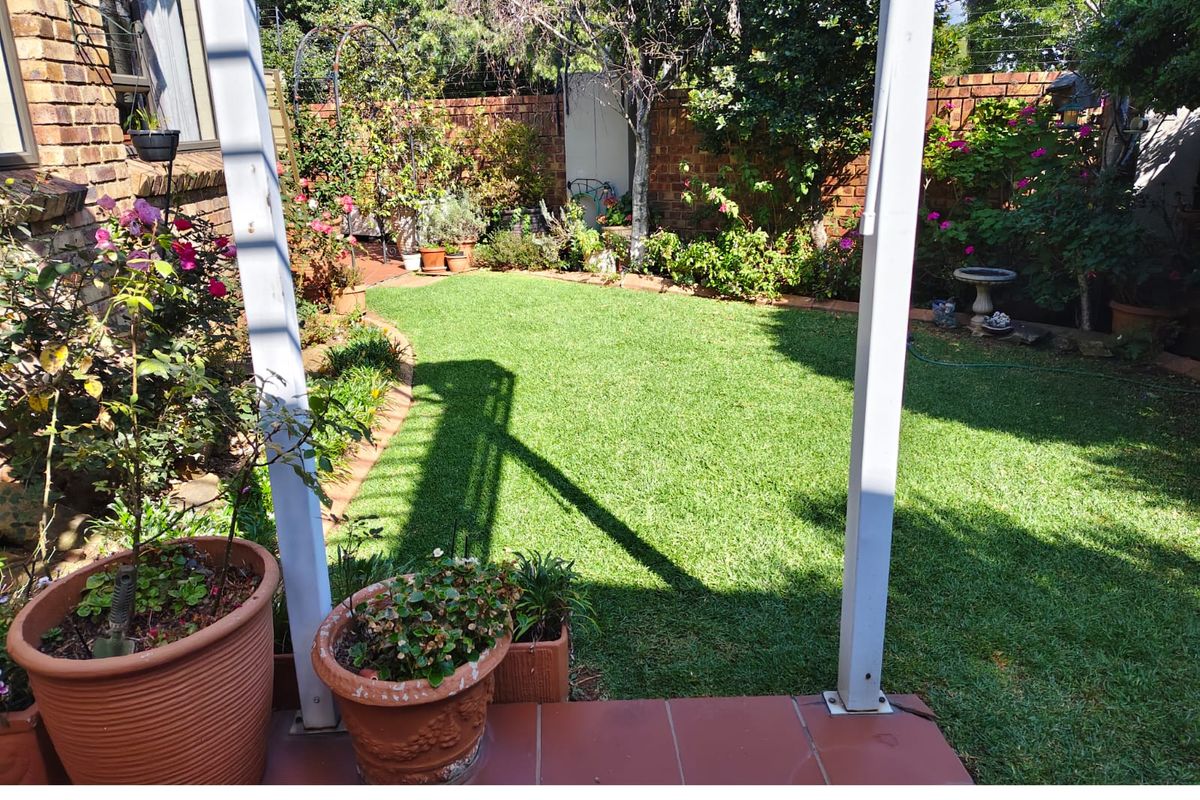 A private rear garden featuring a well-maintained lawn, brick boundary walls, and a paved patio area.