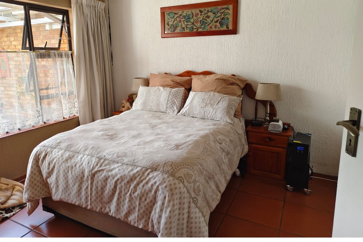 A bedroom featuring terracotta floor tiles, textured walls, and a window overlooking an outdoor area.