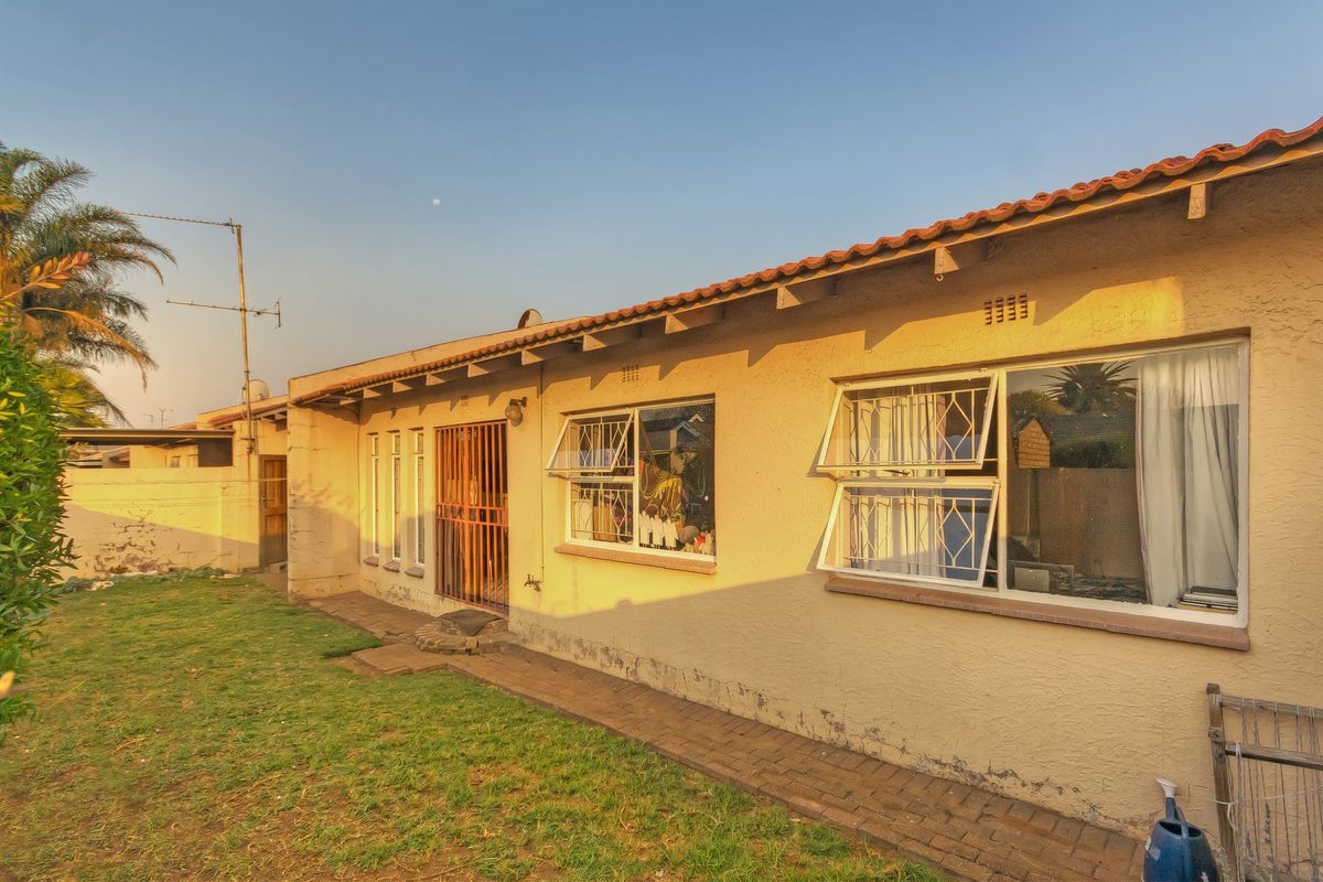 Rear exterior view of the townhouse featuring a paved walkway, lawn area, tiled roof, and security bars on windows and doors.