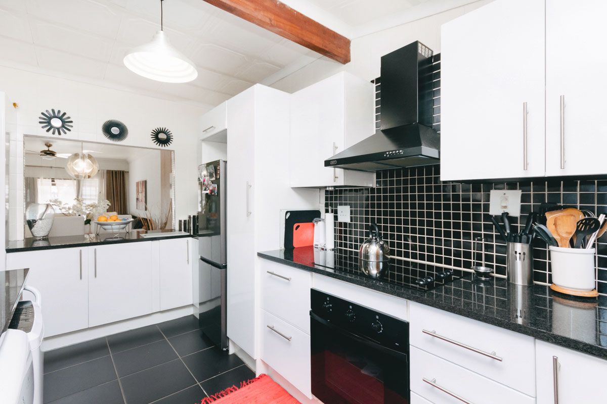 Modern kitchen featuring white cabinetry, black granite countertops, black tiled backsplash, built-in oven, and extractor fan, with an open-plan layout to the living area.