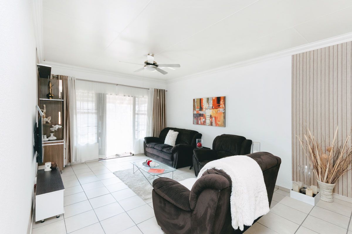 A bright living room featuring tiled flooring, a ceiling fan, and sliding glass doors that provide access to the outdoor area.
