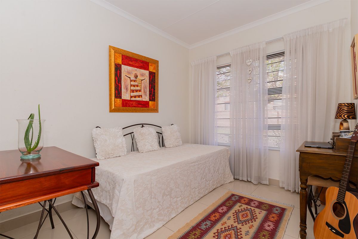 A bedroom featuring tiled flooring, neutral walls, and large windows with fitted blinds and curtains.