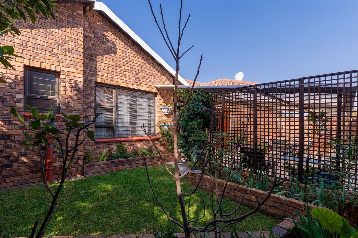 A private rear garden area featuring face-brick exterior walls, a small lawn, raised brick planters, and a decorative privacy screen.