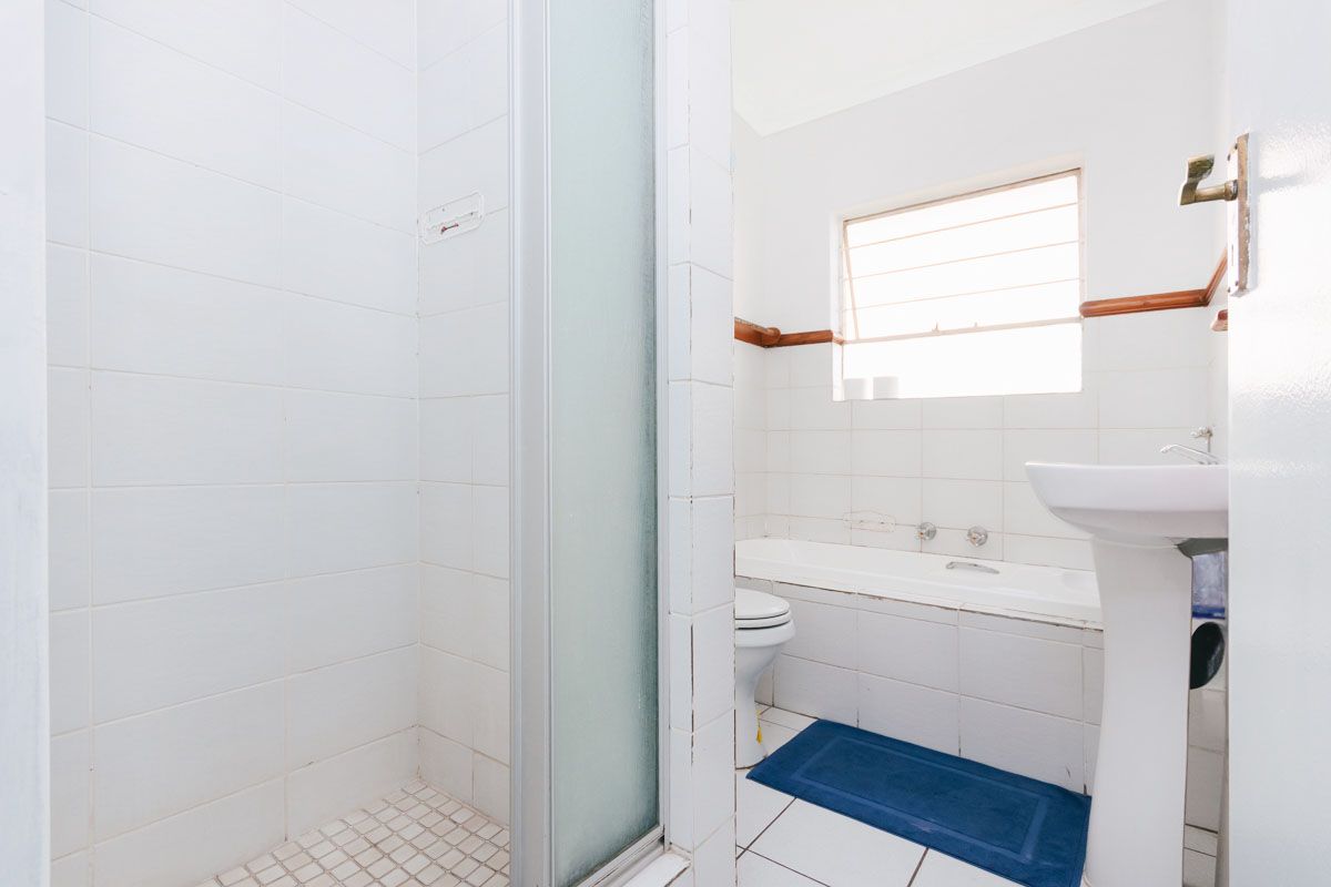 A functional bathroom featuring a separate shower enclosure, a built-in bathtub, and a pedestal basin with white tiled finishes.