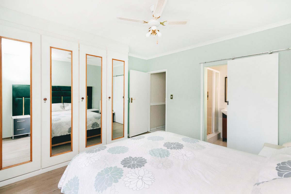 A bedroom featuring built-in mirrored wardrobes, a ceiling fan, and an en-suite bathroom with a sliding door entry.
