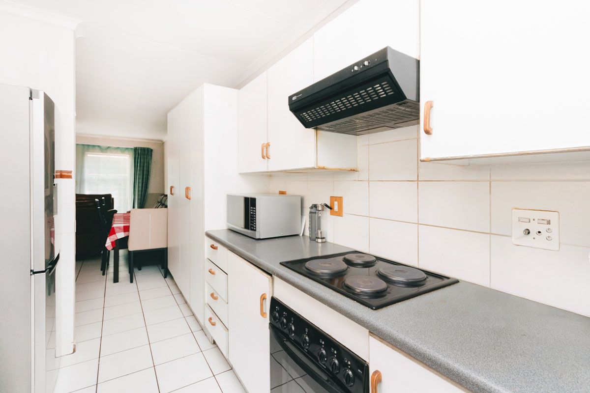 A functional kitchen featuring white cabinetry, a built-in oven, electric hob, and extractor fan, with tiled flooring and direct access to the dining area.