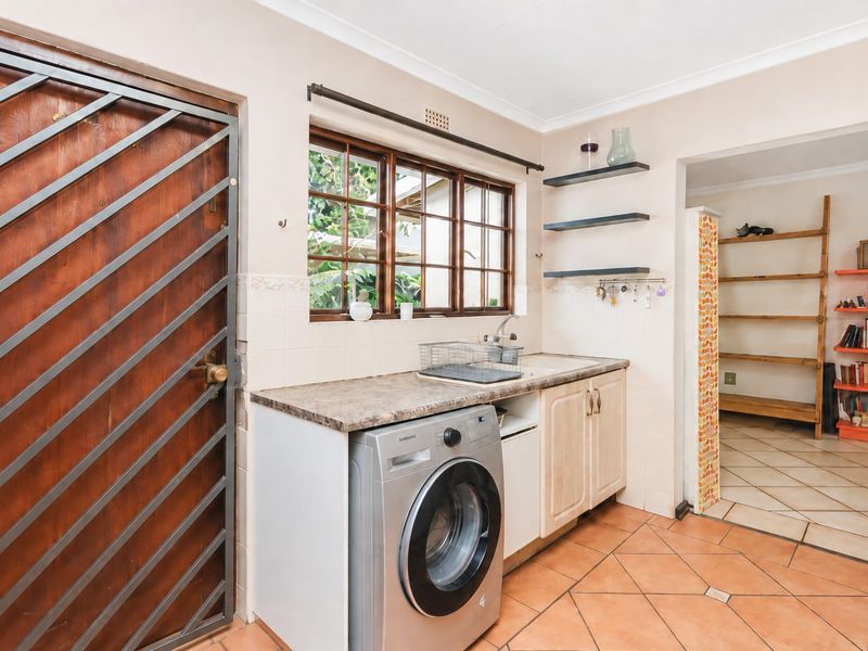 A functional laundry area featuring tiled flooring, built-in cabinetry with a laminate countertop, a stainless steel sink, and a secure timber-framed door.