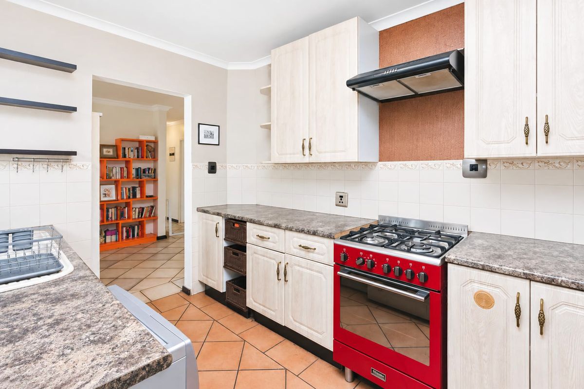 A functional kitchen featuring light-toned cabinetry, laminate countertops, a tiled backsplash, and a prominent red gas stove with an overhead extractor fan.
