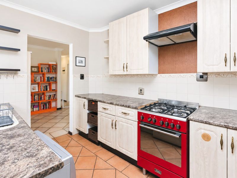 A functional kitchen featuring light-toned cabinetry, laminate countertops, a tiled backsplash, and a prominent red gas stove with an overhead extractor fan.