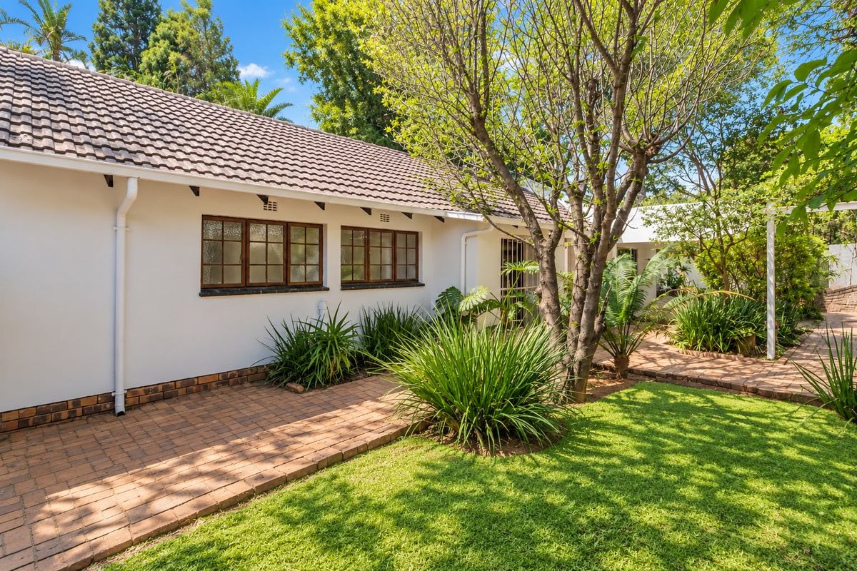 A well-maintained rear exterior view featuring a tiled roof, brick paved pathways, and established garden landscaping alongside the property facade.