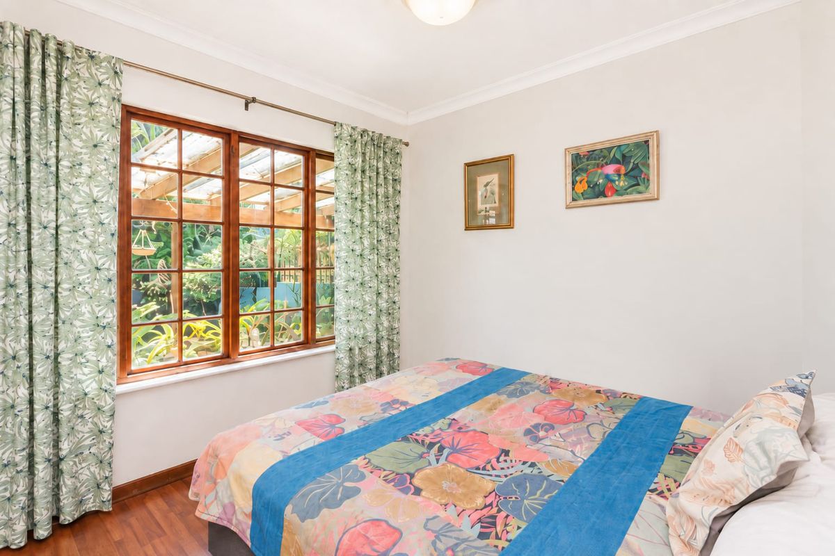 A well-lit bedroom featuring timber-framed windows with garden views, coved ceilings, and laminate flooring.
