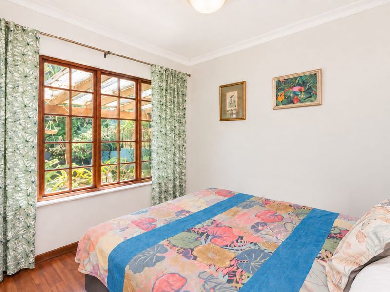 A well-lit bedroom featuring timber-framed windows with garden views, coved ceilings, and laminate flooring.