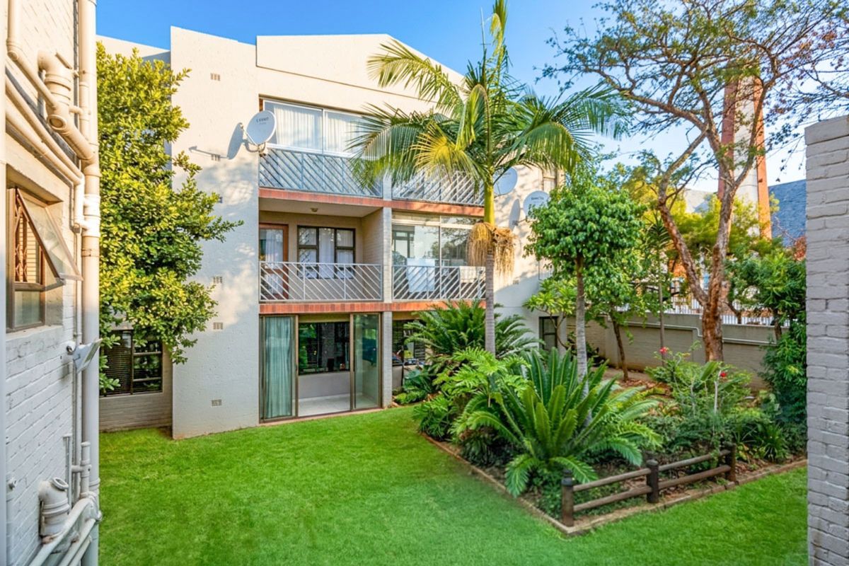 Rear view of a multi-story apartment building featuring private balconies, sliding glass doors, and a well-maintained landscaped garden area.