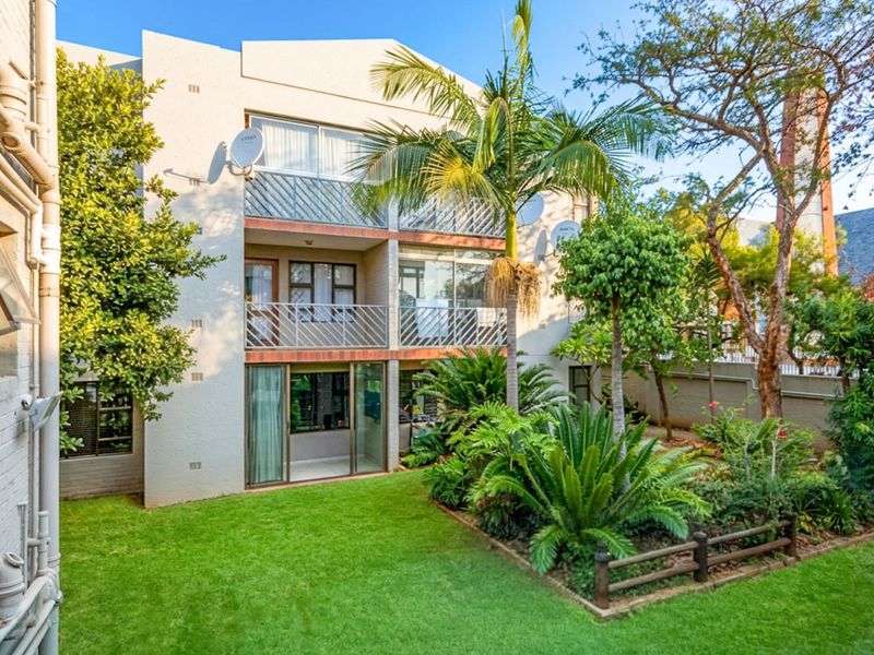 Rear view of a multi-story apartment building featuring private balconies, sliding glass doors, and a well-maintained landscaped garden area.