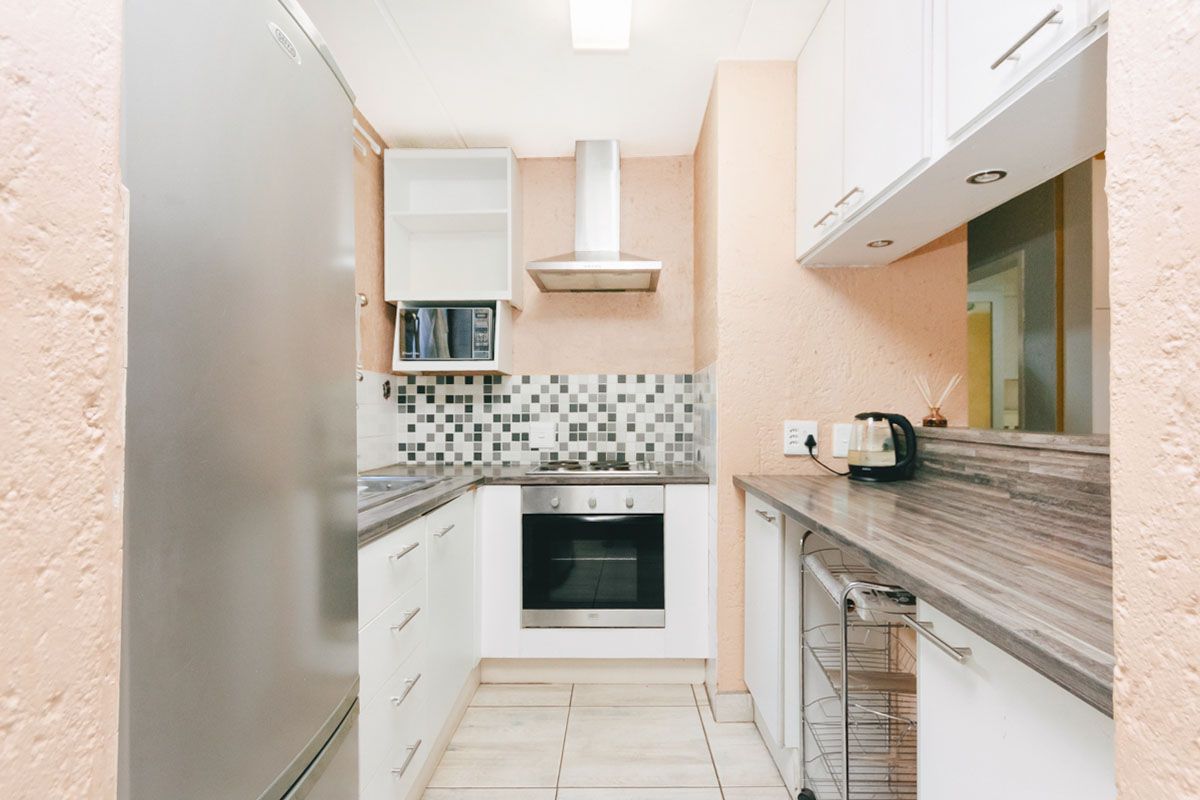 Compact kitchen featuring built-in oven, hob, extractor fan, microwave, laminate countertops, and tiled backsplash with white cabinetry.