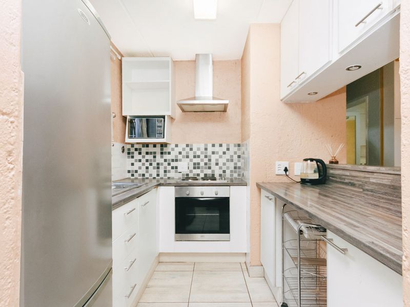 Compact kitchen featuring built-in oven, hob, extractor fan, microwave, laminate countertops, and tiled backsplash with white cabinetry.