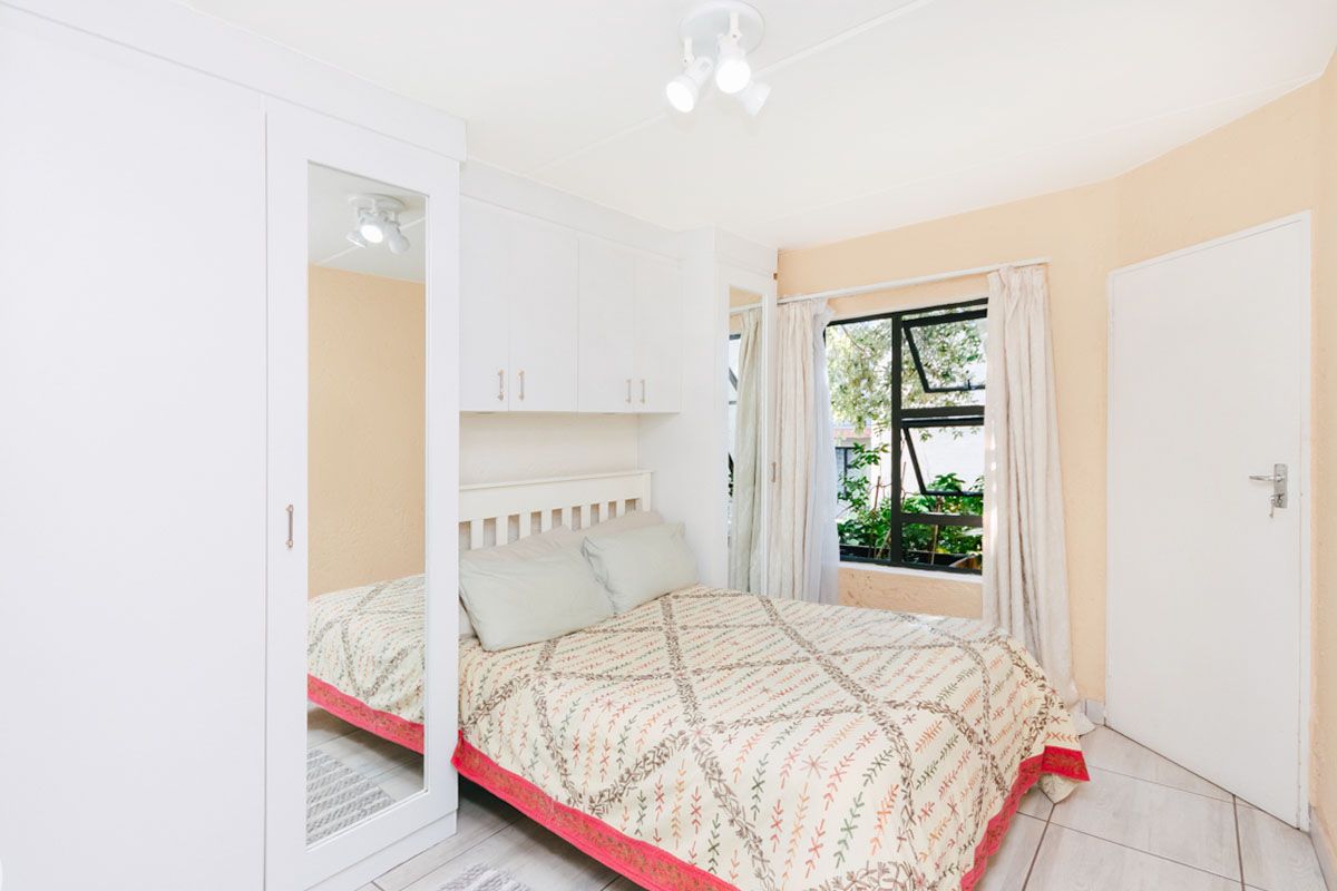A functional bedroom featuring built-in cupboards with mirrored doors, overhead storage, tiled flooring, and a window providing natural light.