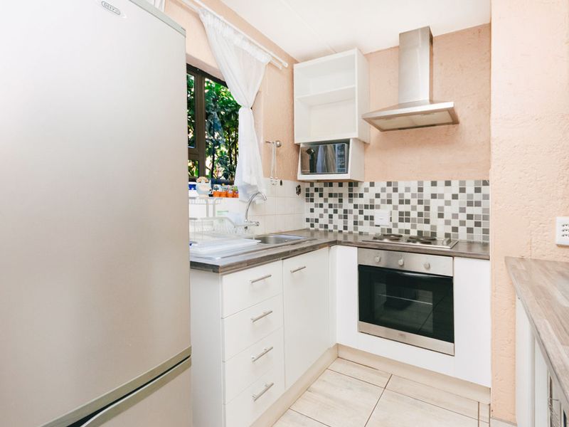 Compact kitchen featuring white cabinetry, a built-in oven with extractor fan, tiled backsplash, and laminate countertops.