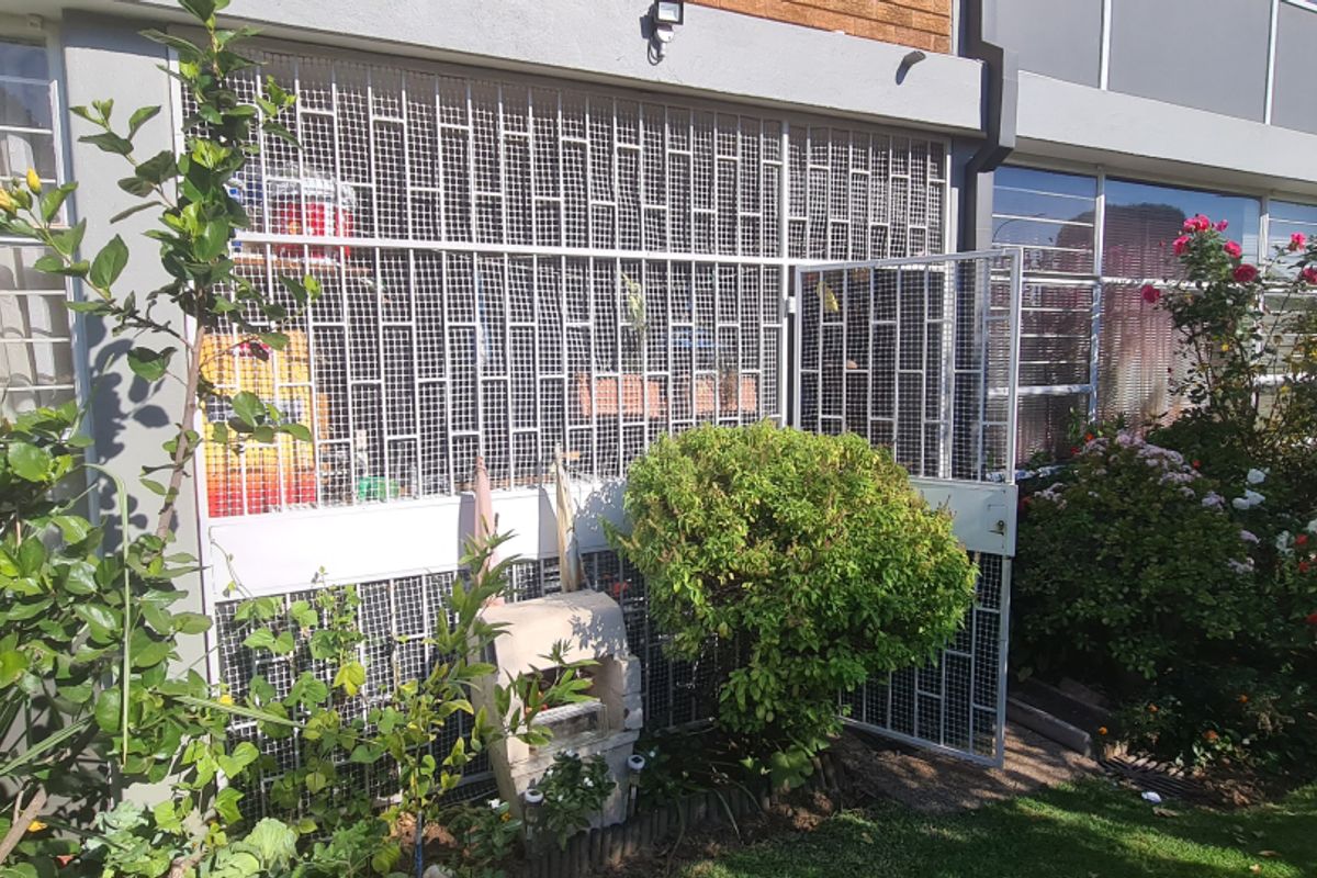 Ground floor exterior view of the flat featuring a private garden area with security bars on windows and a gated entrance.