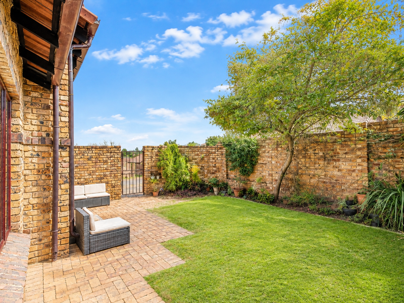 A private rear garden featuring a paved patio area, established lawn, and perimeter face brick walls with a secure metal gate.