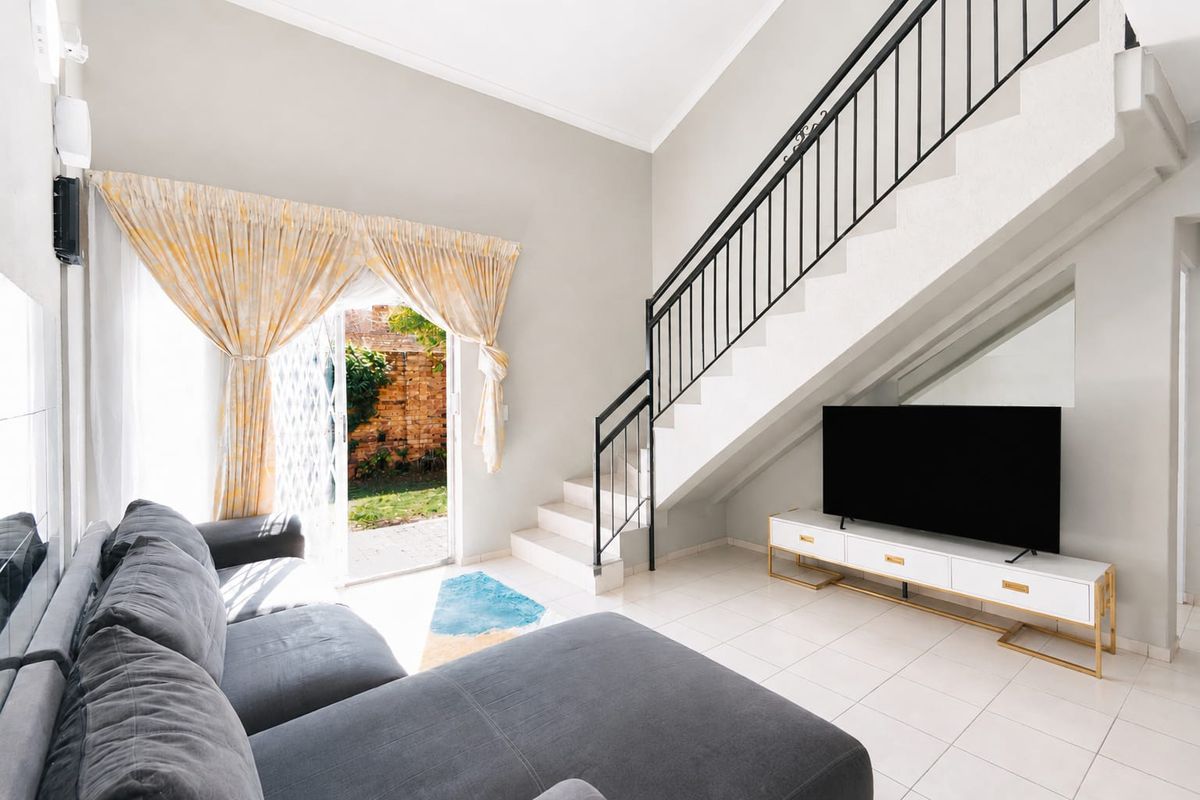 A bright living room featuring tiled flooring, a staircase with a metal balustrade, and a sliding glass door providing access to the rear garden.