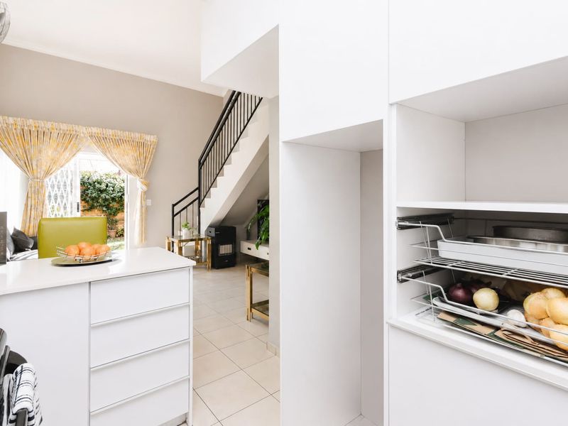 Open plan kitchen area featuring modern white cabinetry, tiled flooring, and a staircase leading to the upper level with access to the outdoor patio.