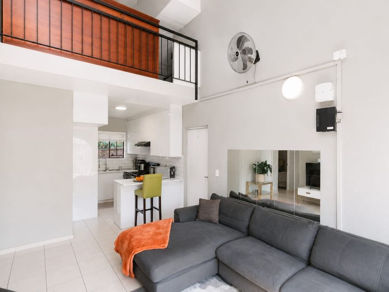 Open-plan living area featuring a modern kitchen with subway tile backsplash, tiled floors, and a mezzanine level with a metal balustrade.