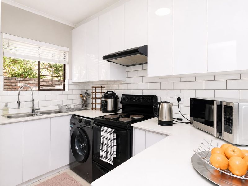 Modern kitchen featuring white gloss cabinetry, subway tile backsplash, quartz countertops, and integrated laundry facilities with a clean, contemporary finish.