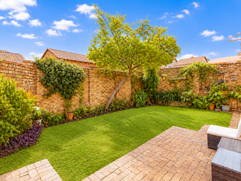 A private rear garden featuring a well-maintained lawn, paved patio area, and established brick boundary walls.