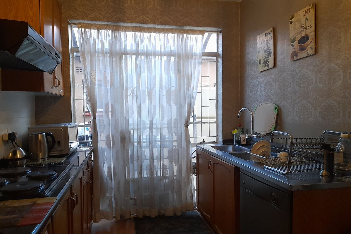 A functional kitchen featuring wooden cabinetry, a built-in hob with extractor fan, and a stainless steel sink, with direct access to an exterior security gate.