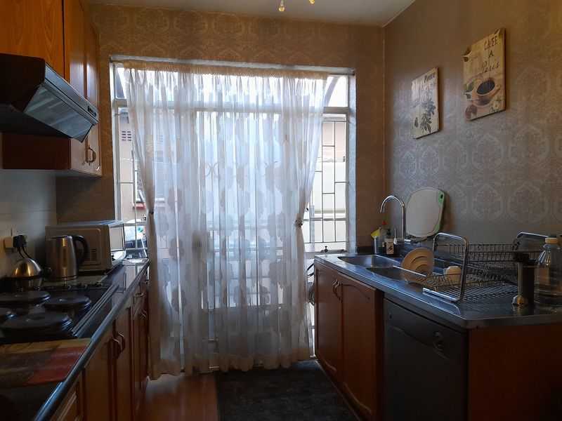 A functional kitchen featuring wooden cabinetry, a built-in hob with extractor fan, and a stainless steel sink, with direct access to an exterior security gate.