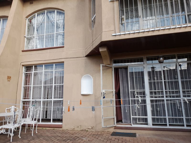 Rear exterior view of a townhouse featuring a paved patio area, security bars on windows and doors, and an arched wall niche.
