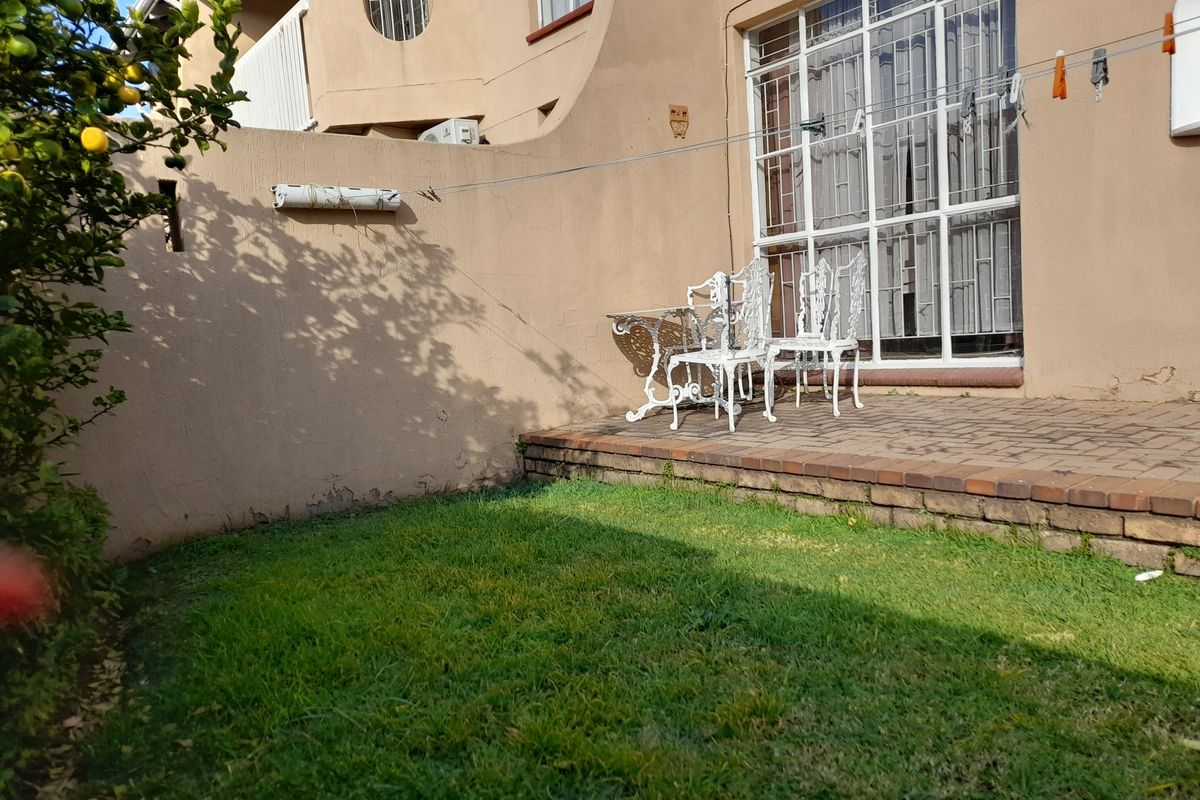 A rear exterior view of the townhouse featuring a small paved patio area, a lawn, and access to the interior via a sliding glass door.