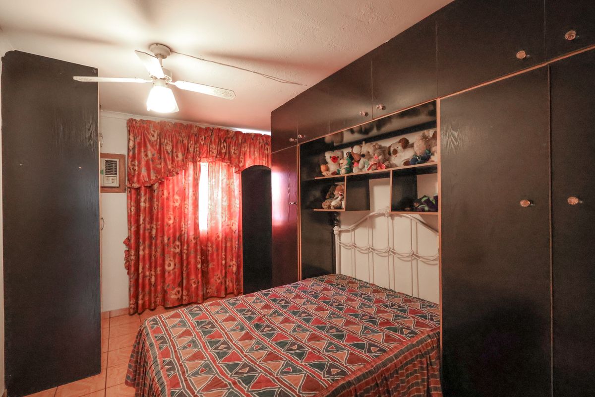 A bedroom featuring extensive dark wood built-in cabinetry, a ceiling fan, and a wall-mounted air conditioning unit with tiled flooring.