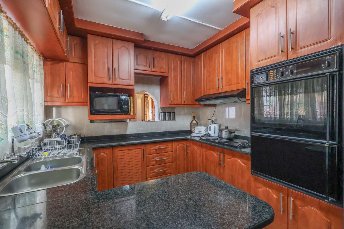 A functional kitchen featuring traditional wooden cabinetry, granite countertops, a double bowl sink, and integrated appliances including an oven and hob.