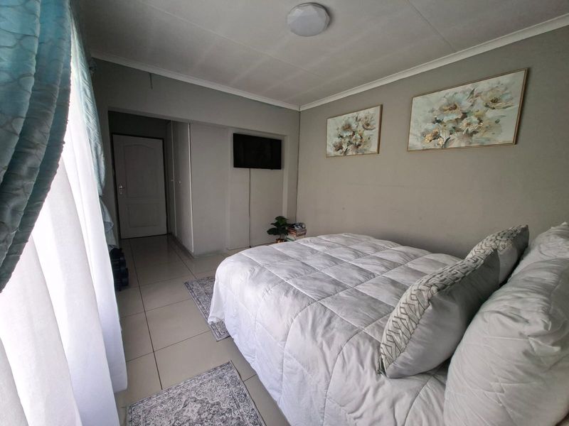 A well-lit bedroom featuring tiled flooring, neutral wall tones, and a built-in doorway leading to the hallway.