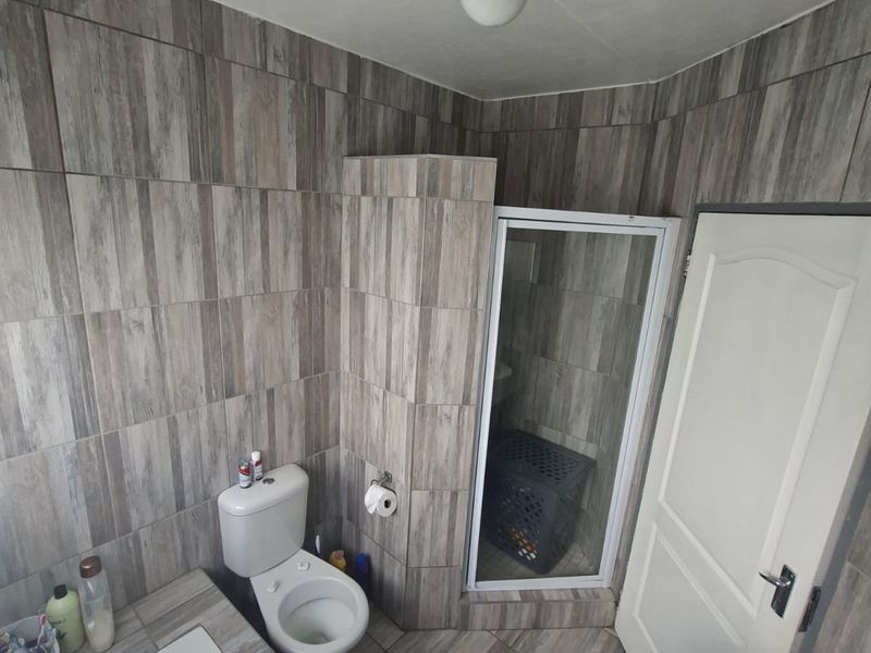A compact bathroom featuring a built-in bathtub, a separate shower enclosure, a toilet, and a modern vessel sink vanity with wood-look wall tiling.