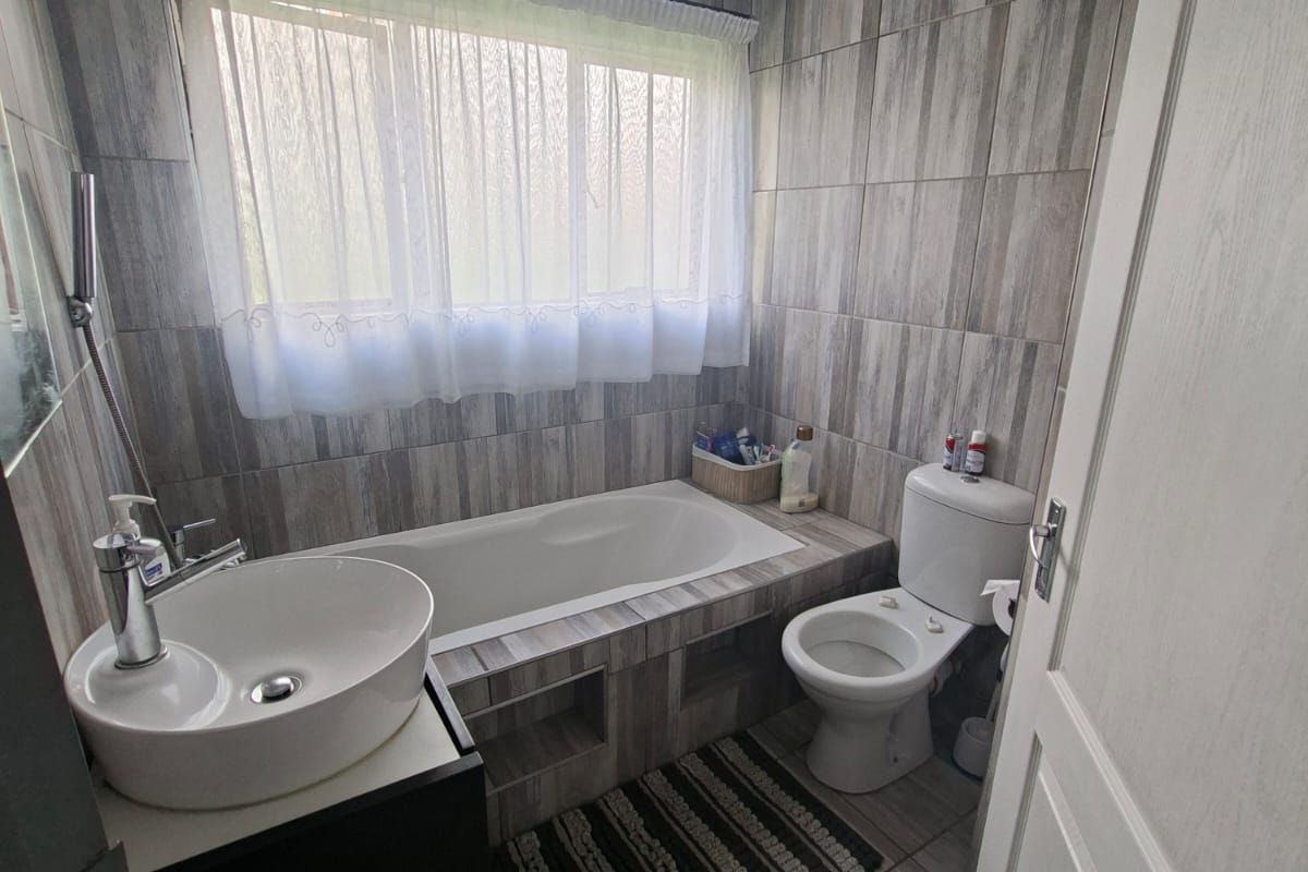 A modern bathroom featuring floor-to-ceiling wood-look tiling, a built-in bathtub, a contemporary vessel sink vanity, and a standard toilet.