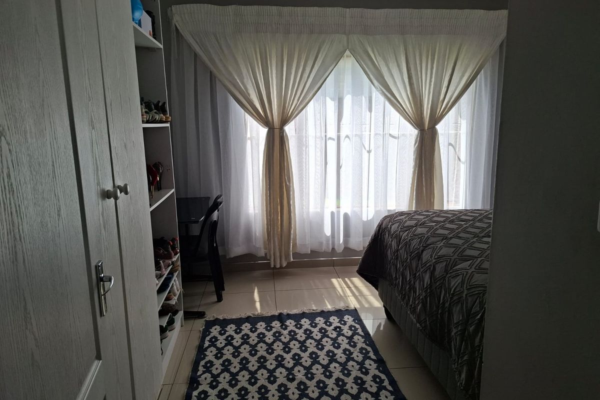 A bedroom featuring tiled flooring, built-in cabinetry, and large windows with curtains, providing a functional and well-lit living space.