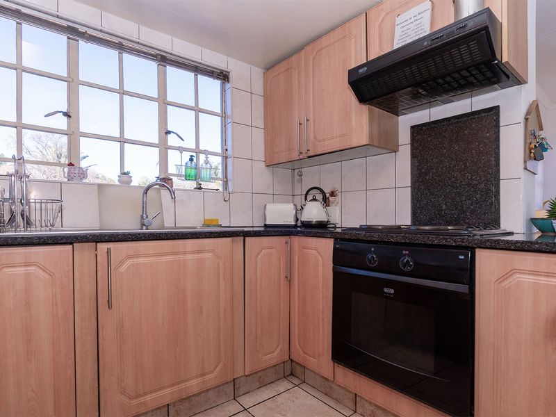 A functional kitchen featuring light wood-finish cabinetry, granite countertops, a built-in oven with extractor fan, and a large window providing natural light.