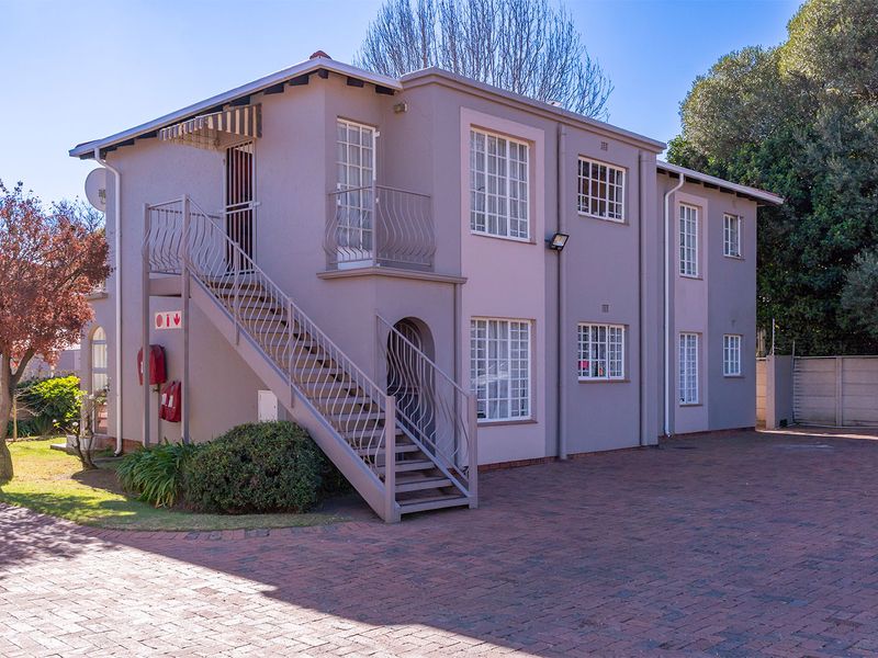 Exterior view of a multi-story apartment building featuring a paved driveway, external staircase with wrought iron railings, and well-maintained facade.