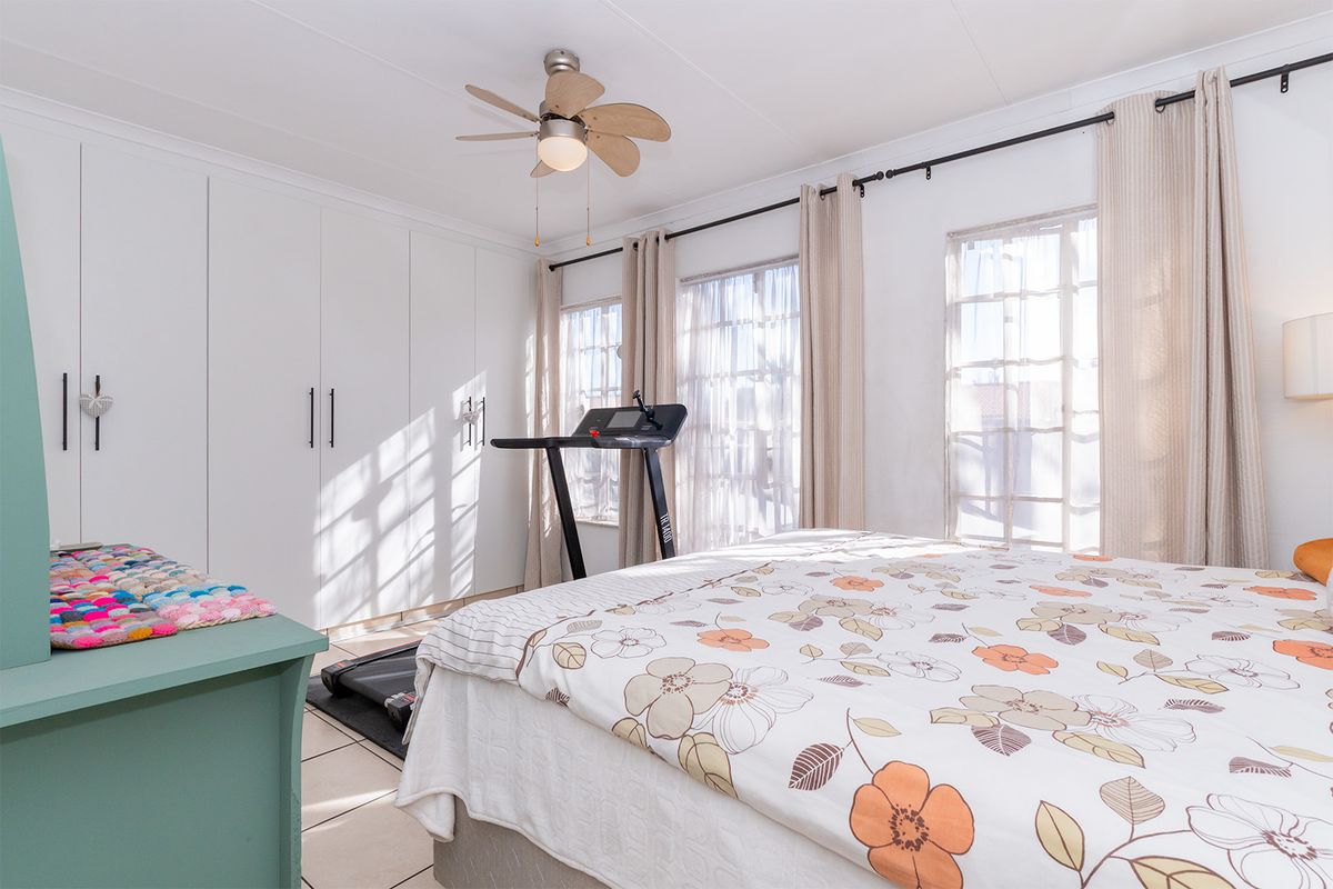 A bright bedroom featuring built-in cupboards, tiled flooring, and a ceiling fan, with large windows allowing for ample natural light.