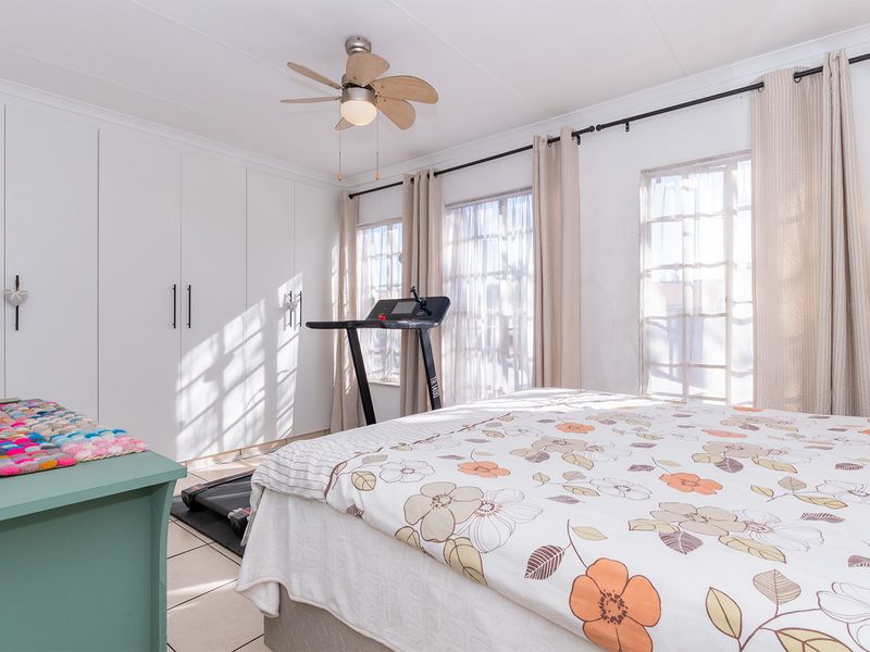 A bright bedroom featuring built-in cupboards, tiled flooring, and a ceiling fan, with large windows allowing for ample natural light.