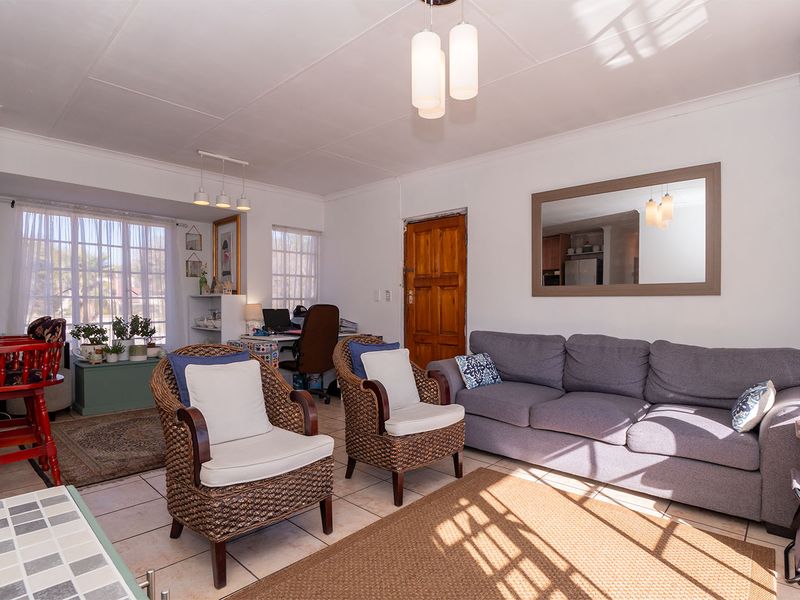 Bright open-plan living area featuring tiled flooring, natural light through large windows, and a solid timber entrance door.