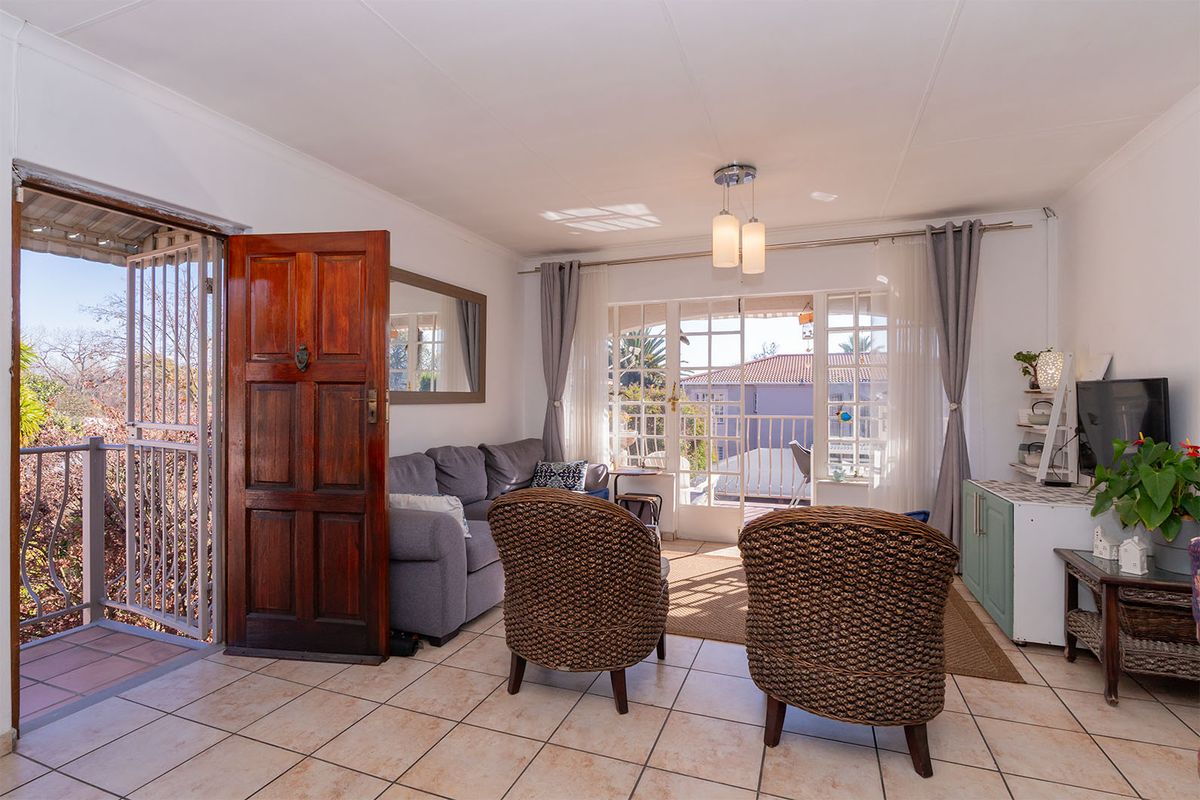 A bright living room featuring tiled flooring, a solid wood entrance door, and glass french doors leading to a balcony.