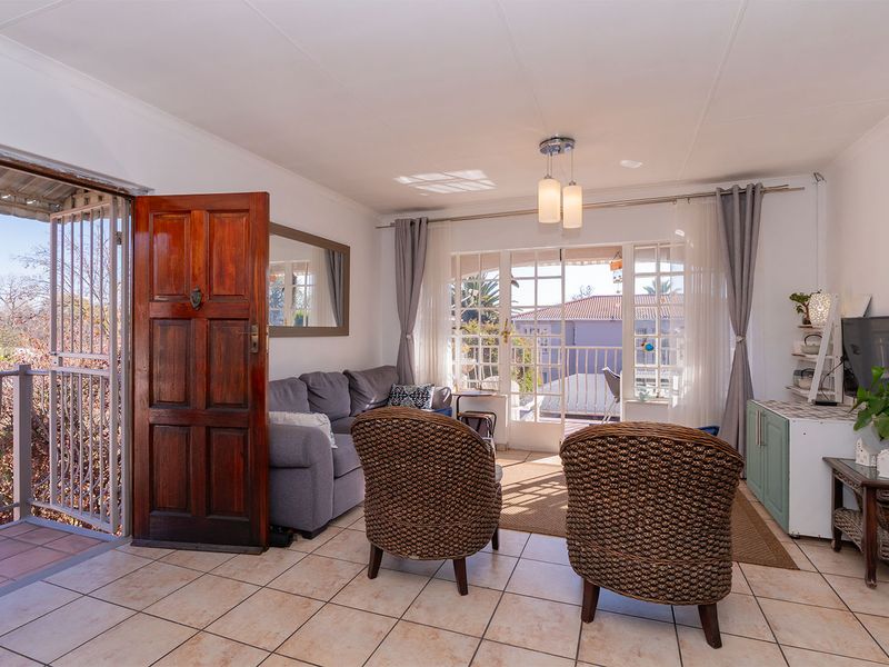 A bright living room featuring tiled flooring, a solid wood entrance door, and glass french doors leading to a balcony.