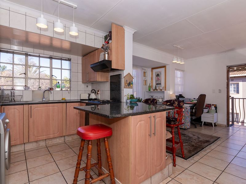 Open-plan kitchen featuring granite countertops, laminate cabinetry, and tiled flooring, seamlessly flowing into the adjacent living area with access to a balcony.