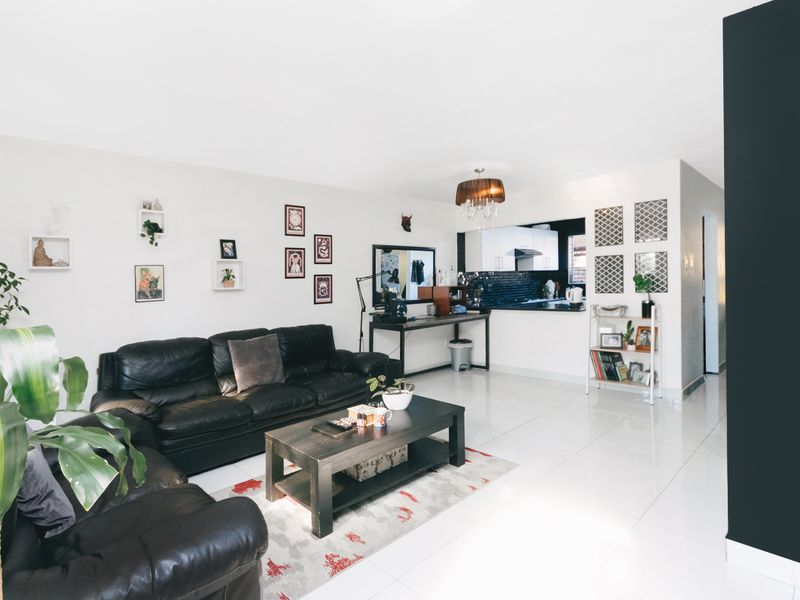 Open-plan living area featuring polished tiled floors, a modern kitchen pass-through window, and neutral wall finishes.
